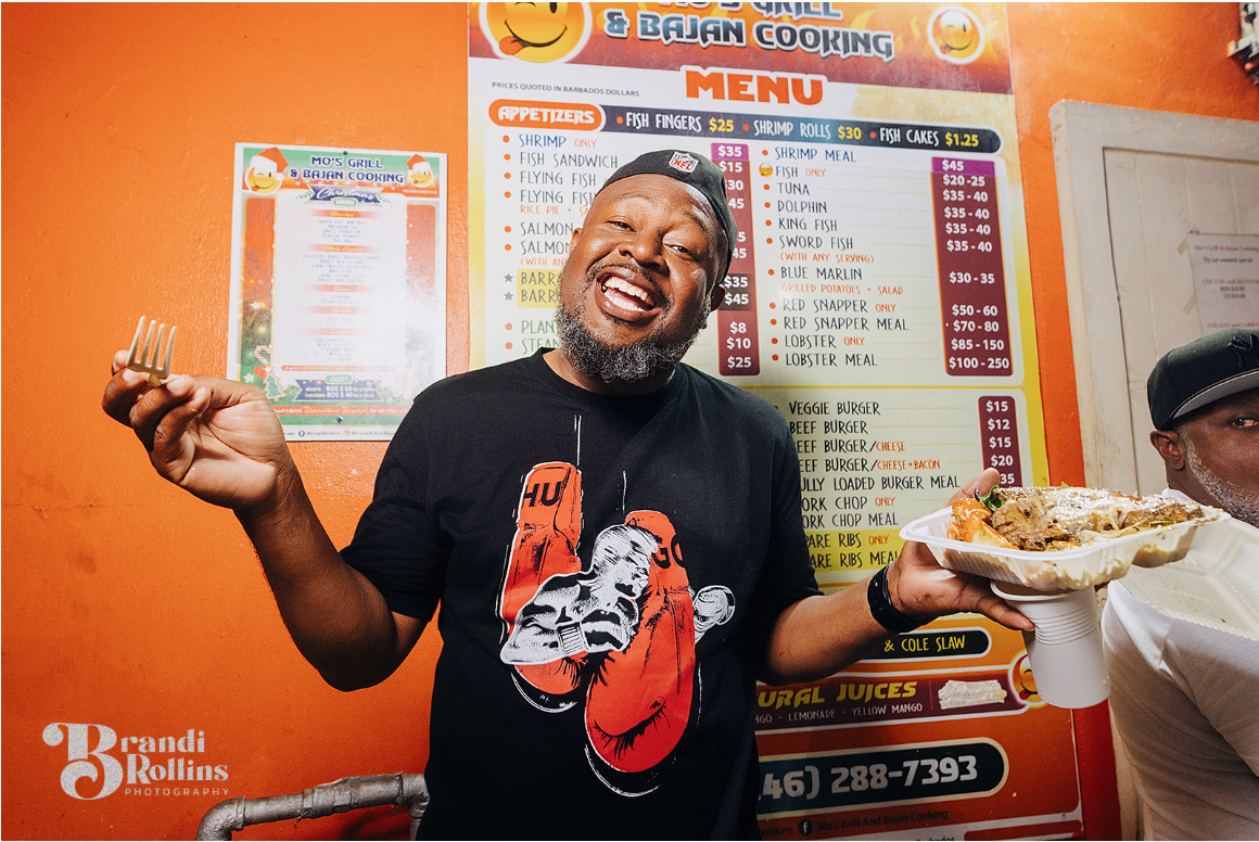 A guest laughing with a plate of freshly grilled Bajan food at Oistins Fish Fry