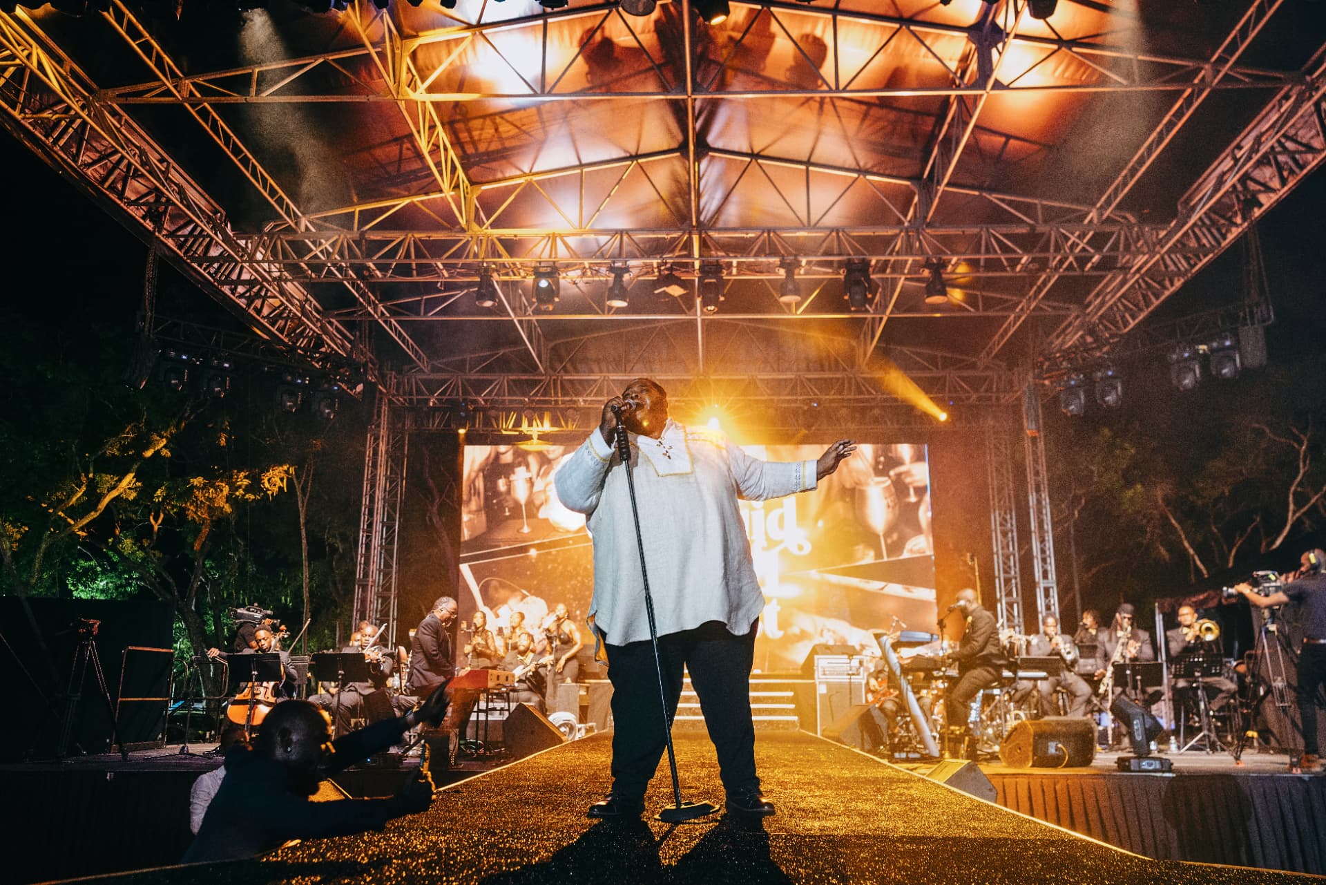 A singer performing with a live orchestra at the Liquid Gold Feast Finale