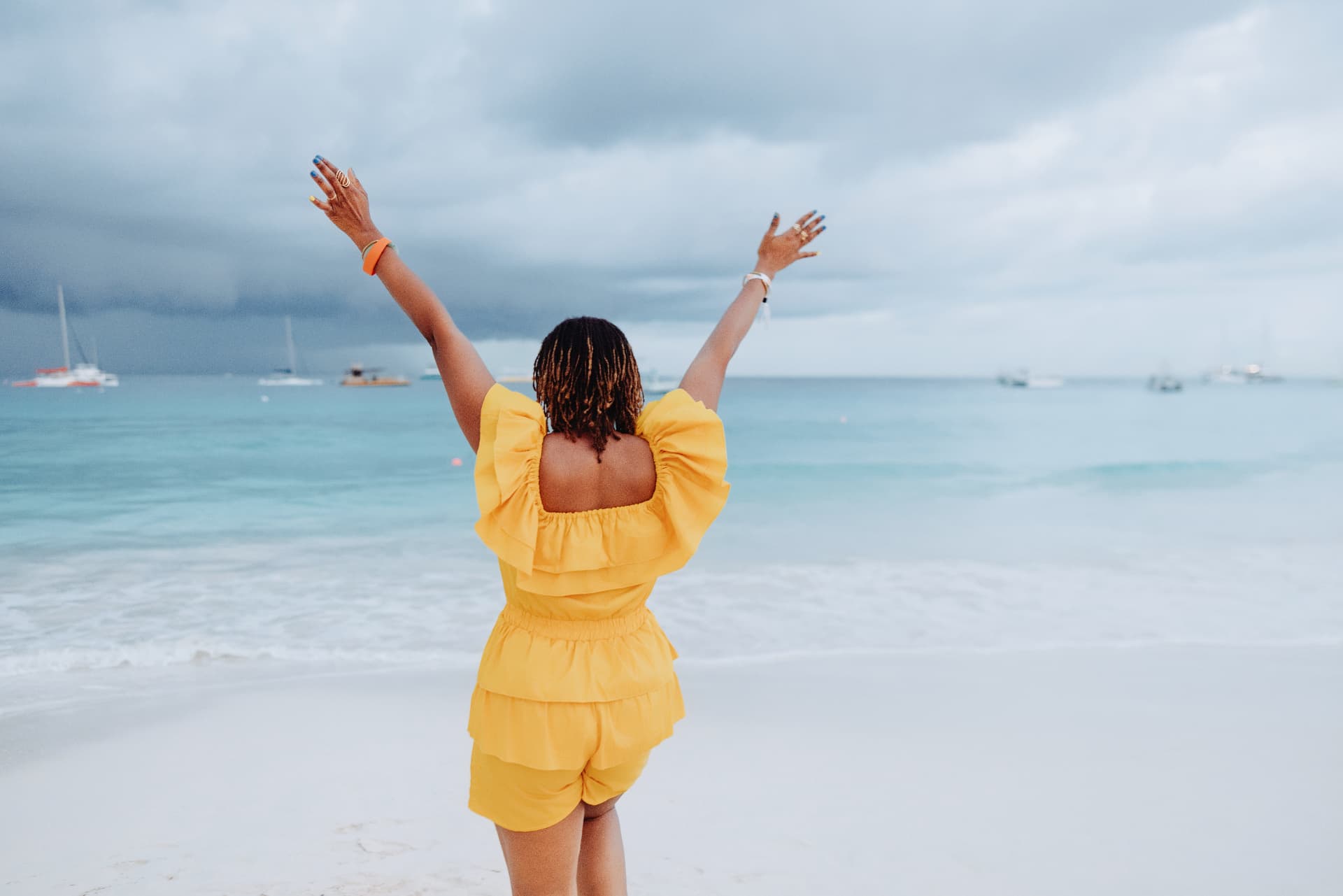 A traveler in a yellow outfit facing the Barbados sea with her arms raised