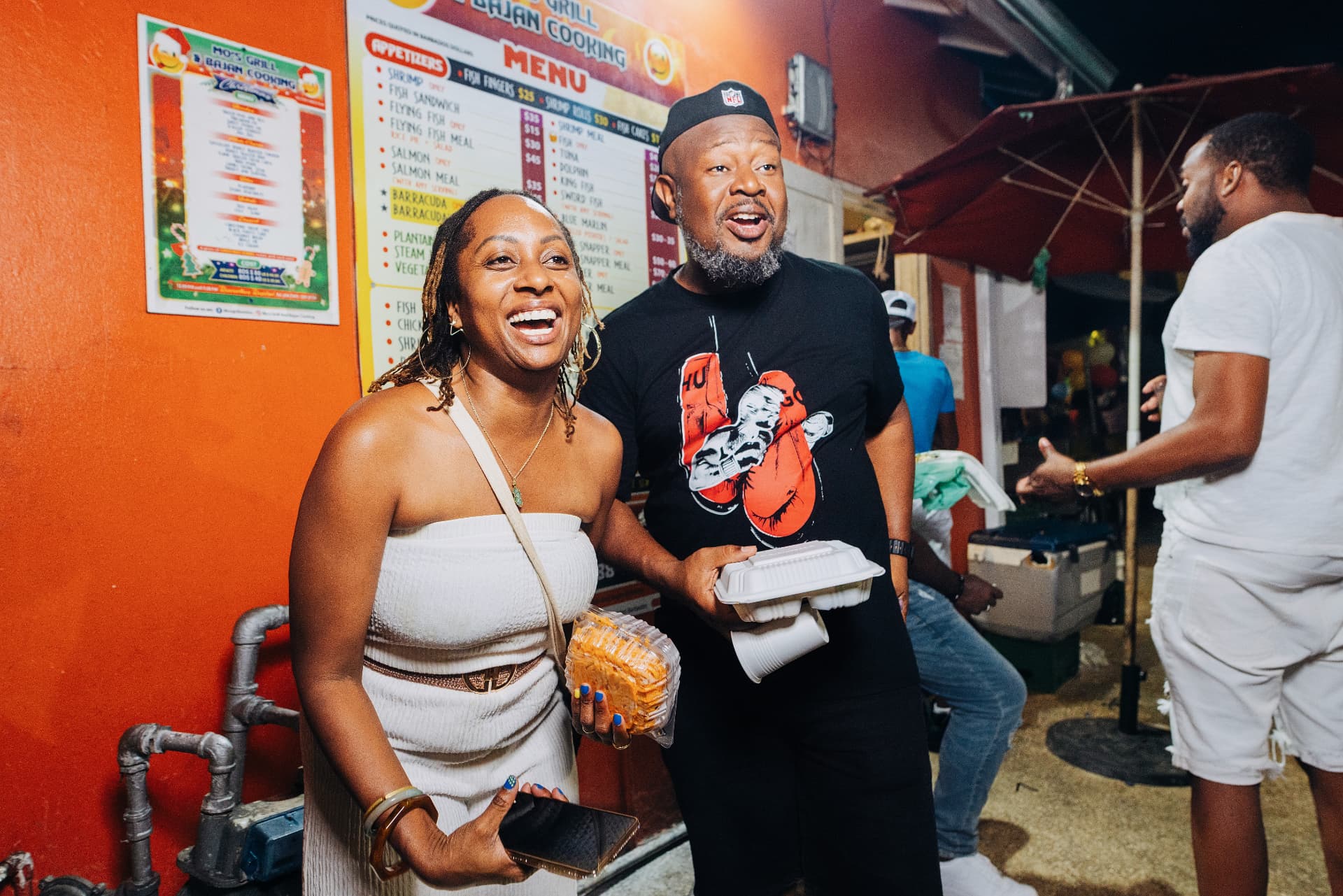 Travelers laughing with fresh Bajan food outside a local grill at Oistins